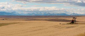 A lone oil rig on grasslands with a view of the mountains in the distance